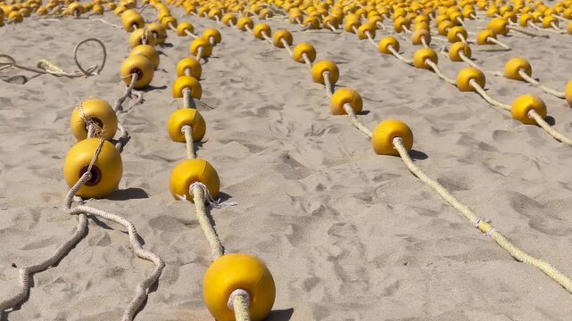 Close up Rows of Yellow Buoys on braided rope neatly laid out in parallel and Stretching Into Distance on the sand of the Beach. Cinematic panoramic shot