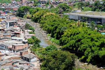 Fototapeta premium Aerial view of the Otún River flowing through Dosquebradas and Pereira, Colombia, with dense neighborhoods and green riverbanks
