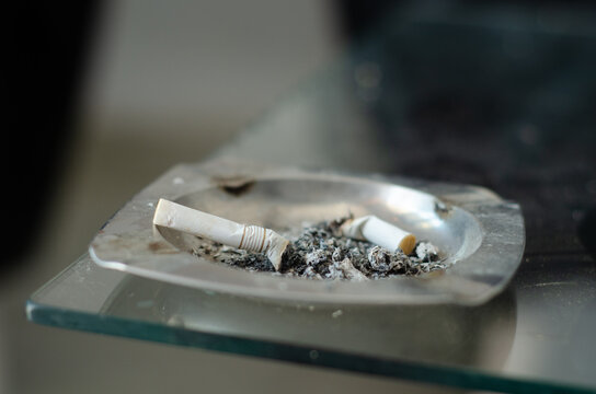 Two Cigarette Butts and Ash in a Metal Ashtray on a Glass Surface