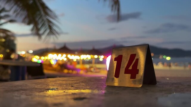 Close up of Table number fourteen sign on beach cafe table at night. Client waiting for order