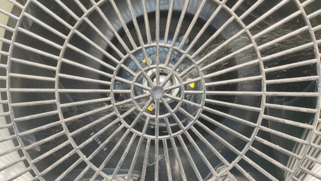 Close-up of a circular air conditioner fan grill cover with symmetrical radial patterns. Concept of HVAC system, industrial hardware, cooling equipment, and geometric texture background