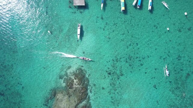 Top down aerial view of speedboat crossing clear turquoise tropical sea over shallow reef near Labuan Bajo Indonesia. Not AI-generated.