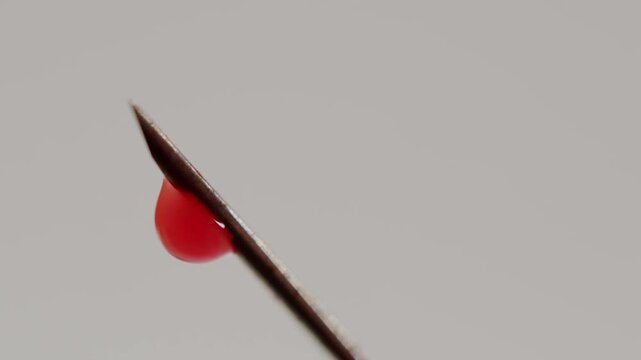 Macro view of a red blood drop falling from the tip of a hypodermic needle isolated on a clean white background, medical procedures, Blood drop dripping from a needle tip on white background.