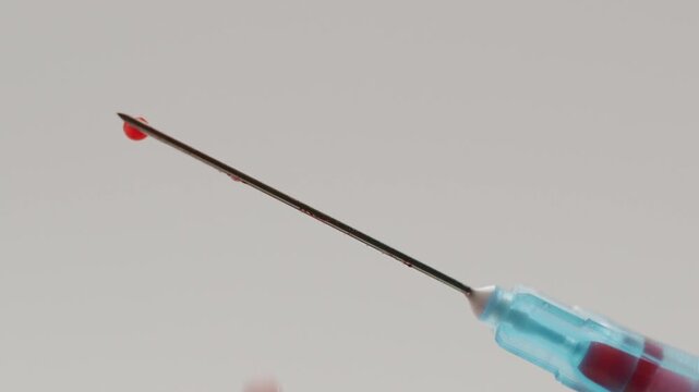 Close-up view of a single red drop of blood forming and falling from the tip of a syringe needle, symbolizing medical procedures, blood donation, Drop of blood falling from a hypodermic