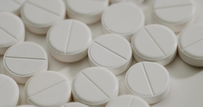 Macro view of many white round scored medical tablets slowly rotating on a clean surface, representing pharmaceutical production, healthcare treatment, and the concept of addiction or overdose