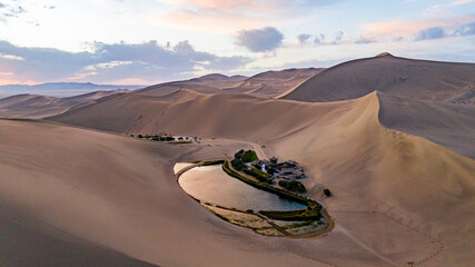Aerial view of Crescent Lake (Yueyaquan) surrounded by the towering sand dunes of Mingsha Mountain at sunset in Dunhuang, Gansu, China © Isabel