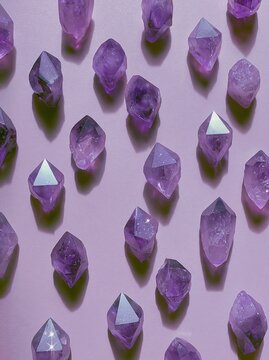 Collection of naturally occurring purple amethyst crystal points arranged in a decorative pattern on a light pink background