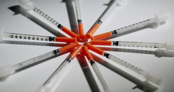 Many medical insulin syringes with orange caps rotating in a circle on an isolated white background, representing diabetes management, healthcare, and medical treatment concepts.