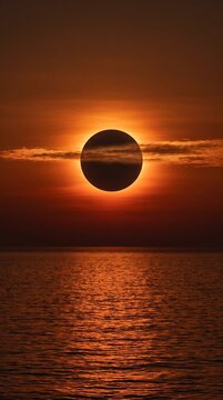 Total solar eclipse casts a mesmerizing dark silhouette against the fiery sunset sky over the tranquil ocean horizon, creating a breathtaking celestial spectacle