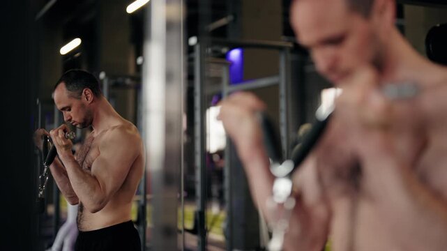 Determined adult athlete with a muscular torso performing a standing bicep curl exercise on a cable crossover machine during an intense strength training session in a modern fitness center