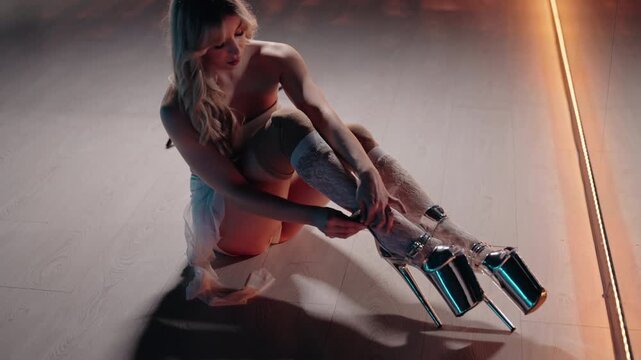 High angle view of a beautiful blonde dancer in lingerie sitting on the floor and fastening her platform stiletto heels, preparing for a striptease or pole dance performance