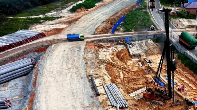 Aerial drone view of a heavy piling machine operating on a large civil construction site with stacked concrete piles.