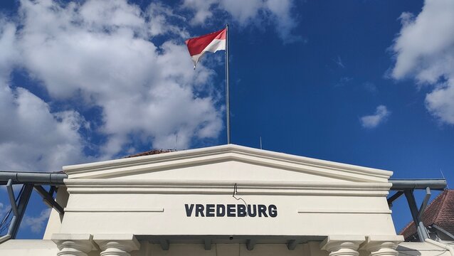 Historic Vredeburg fort building facade with an Indonesian flag flying under a cloudy blue sky. Concept of national heritage, colonial architecture landmark, and tourism photography.