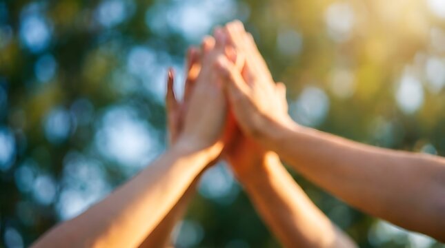 Diverse group of hands raised in a high five outdoors in bright sunlight