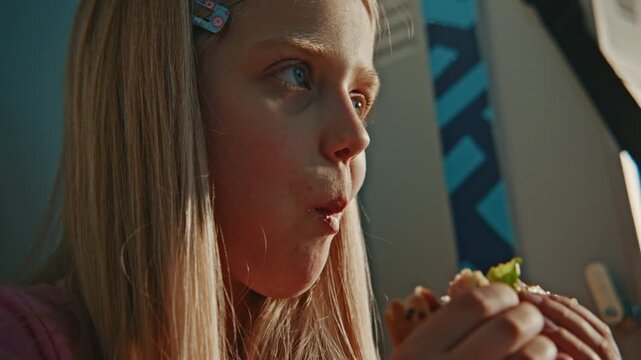 Close Up of Blonde Girl Having Nutritious Lunch Heartily in Sunny School Corridor Near Metal Lockers. Concept of Eating Habits, Education, School Nutrition, Childhood, and Modern School Environment.