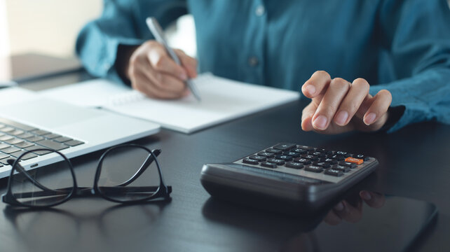 Close up of business woman using calculator to calculate and writing note, accounting. Doing finance, budgeting and tax calculation