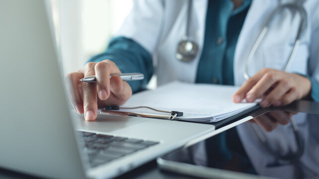 Doctor working on laptop and preparing patient's information for meeting with medical team. 