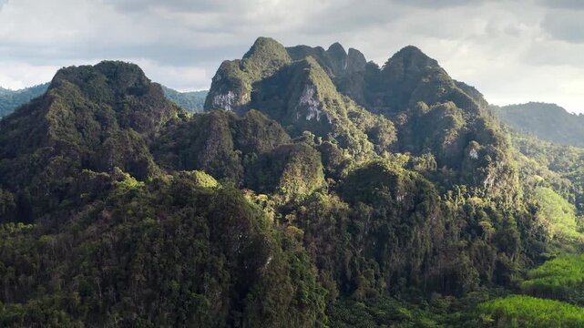 Dense rainforest covers limestone karsts, creating a dramatic tropical landscape in famous KHAO SOK National Park, a popular travel destination in southern Thailand. Aerial view drone flight panorama