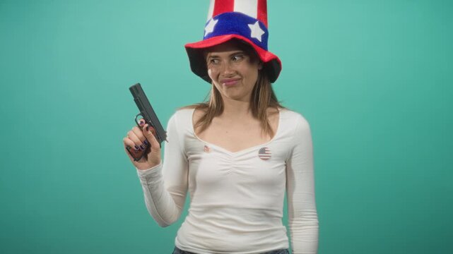 Woman holding pistol in right hand, smirking with finger near trigger in studio wearing tall us star hat and flag pin on shirt; satire patriotism.
