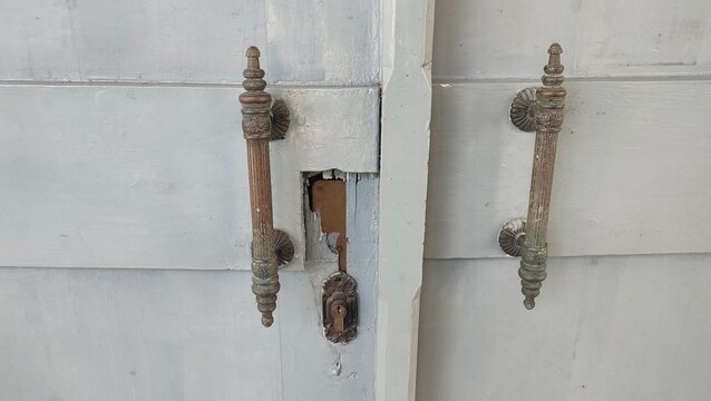 Antique classic metal door handles on a grey wooden double door. Concept of vintage architectural hardware design, historic building interior, and heritage photography.