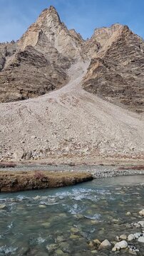 Majestic Gonbo Rangjon monolithic peak with clear glacial river flowing through rocky terrain in Zanskar valley, Ladakh.