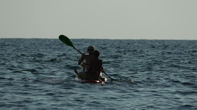 Kayaking paddling ocean two tourists silhouetted enjoying sea sport adventure against a bright summer sky