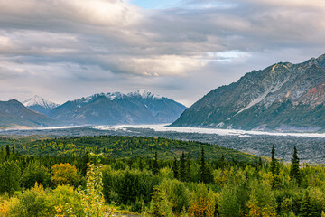 Fototapeta premium A braided glacial river winds through a forested valley flanked by rugged Chugach peaks.