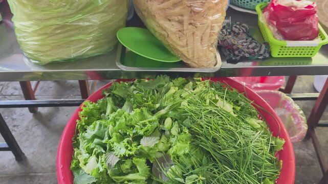 High angle shot of a large red basket filled with fresh raw mixed vegetables, herbs, and chives for Vietnamese street food