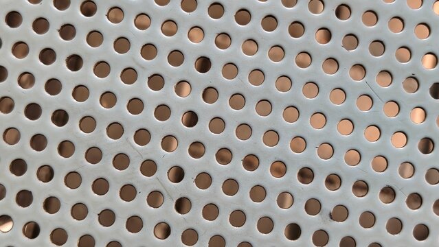 Macro close-up photograph of a grey perforated metal sheet with small round holes arranged in a uniform grid pattern. Industrial texture background.
