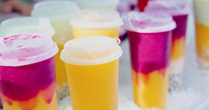 Fruit bubble tea cups standing on ice bed, outdoor street food market stall, refreshing summer beverages with tapioca pearls, commercial beverage photography.