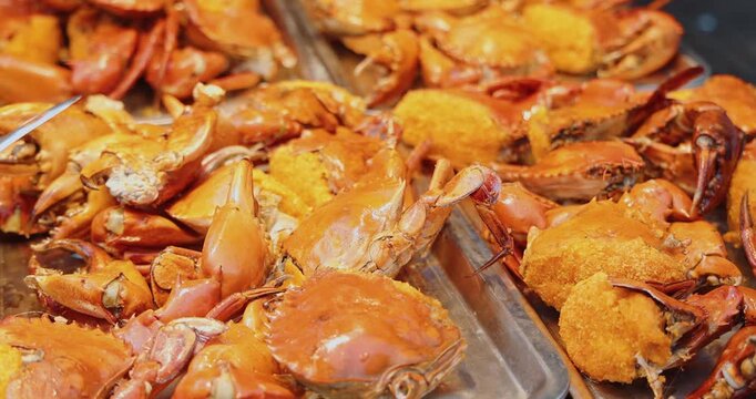 Cooked mud crabs (Scylla serrata) with orange roe displayed on metal trays at a busy street food market, traditional Asian seafood cuisine, commercial food stall background.