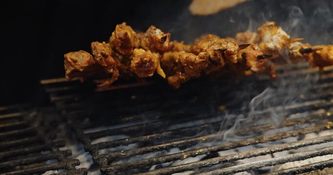 Meat skewers brushing sauce on charcoal grill, traditional street food preparation at night market stall, culinary travel documentary.