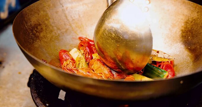 Crawfish being stirred in large metal wok with ladle, spicy seafood preparation in street food kitchen, professional culinary documentary.