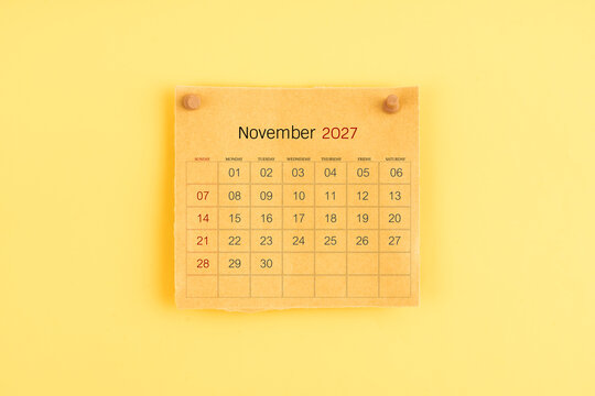 November 2027 brown calendar with wooden thumbtack on yellow background.