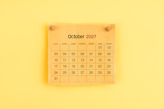 October 2027 brown calendar with wooden thumbtack on yellow background.