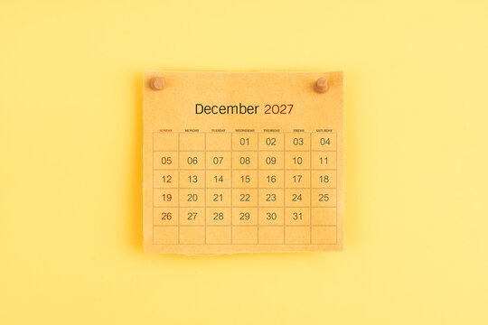 December 2027 brown calendar with wooden thumbtack on yellow background.