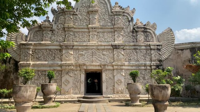 Historic entrance gate of Taman Sari Water Castle in Yogyakarta with intricate carved stone ornaments, green trees, and blue sky.