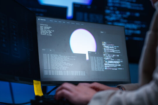 A blond male network security analyst points at the terminal explaining the output at a multi-monitor workstation in a darkened control room, defending the corporate network.
