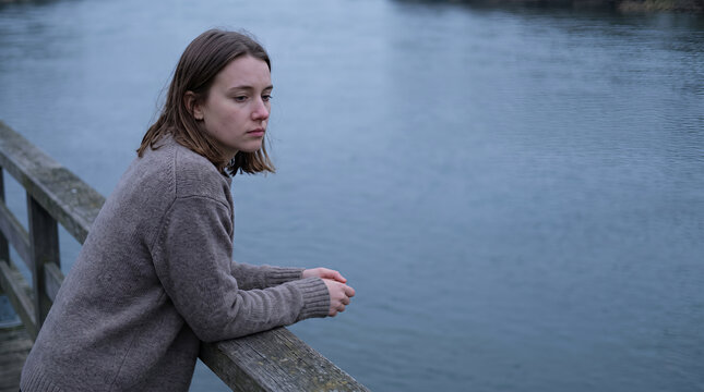 Woman sitting thoughtful on dock overlooking calm water