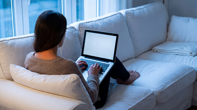 Woman working on laptop computer while sitting on comfortable sofa