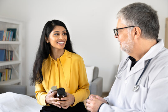 South Asian woman holding medicine bottles, discussing prescribed medications dosage, listening health recommendations, talking with doctor in medical clinic. Healthcare services, patient consultation