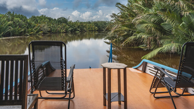 The traditional Indonesian boat klotok floats on the river in the jungle. Deck chairs, a table on board.There is a riverbed ahead, thickets of palm nypa fruticans on the banks.Blue sky, clouds. Borneo