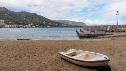 Small rowing boat resting on sandy beach near stone pier in Cefalu, Sicily, Italy © Eleseus