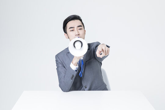 Businessman with megaphone pointing forward at desk in white studio