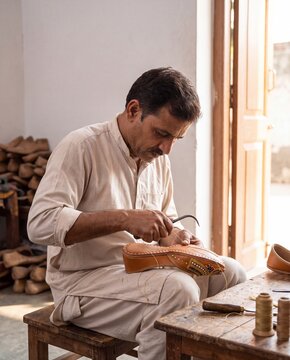 Artisan hand stitching traditional embroidered leather jutti shoes in workshop