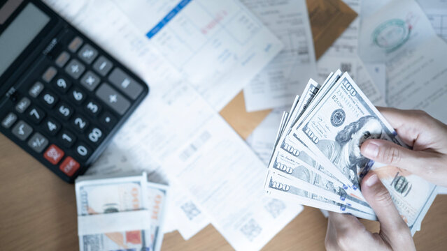 Top view of hands counting US dollar banknotes with calculator, bills and financial documents on desk, concept of household expenses, budgeting, debt, payment and money management.