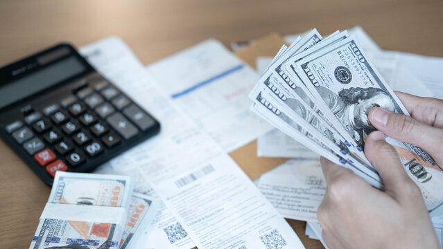 Close-up of hands counting US dollar banknotes over bills and financial documents with calculator, representing budgeting, expenses, debt, payment, accounting and personal finance.
