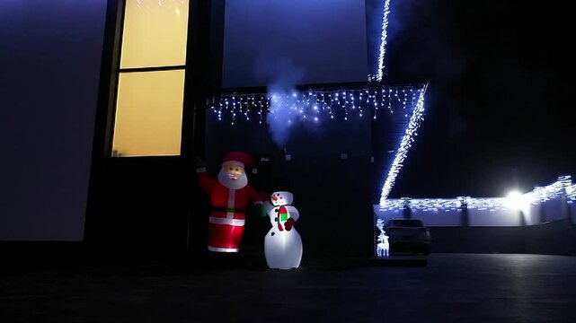 Night lights glow softly around a modern house. Santa figure stands near the entrance, glowing warmly. Smoke curls gently around the festive lights. Cozy holiday ambiance sets the scene