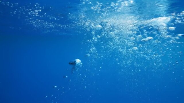 Diver ascending through luminous blue ocean bubbles with sun rays filtering from above