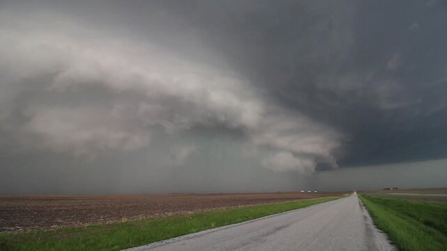 A dangerous severe storm with lightning and hail approaches along a dirt road in the countryside.
